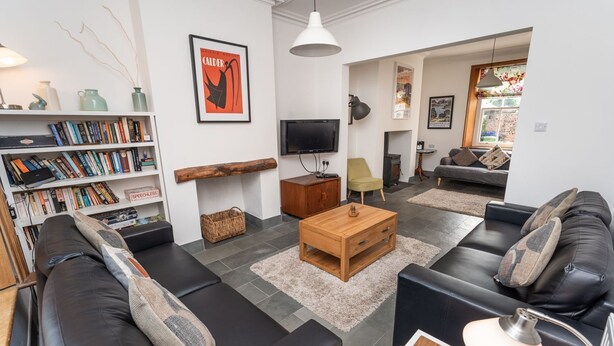 A modern living room with black leather sofas, a wooden coffee table, a bookshelf, a television, and a fireplace. - Coleridge Cottage -  a cottage that sleeps 5 guests  in 3 bedrooms (Central Keswick)