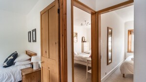 A bedroom with a wooden wardrobe, a bedside table with a lamp, a bed with white bedding, and a mirror on the wall. - Coleridge Cottage -  a cottage that sleeps 5 guests  in 3 bedrooms (Central Keswick)