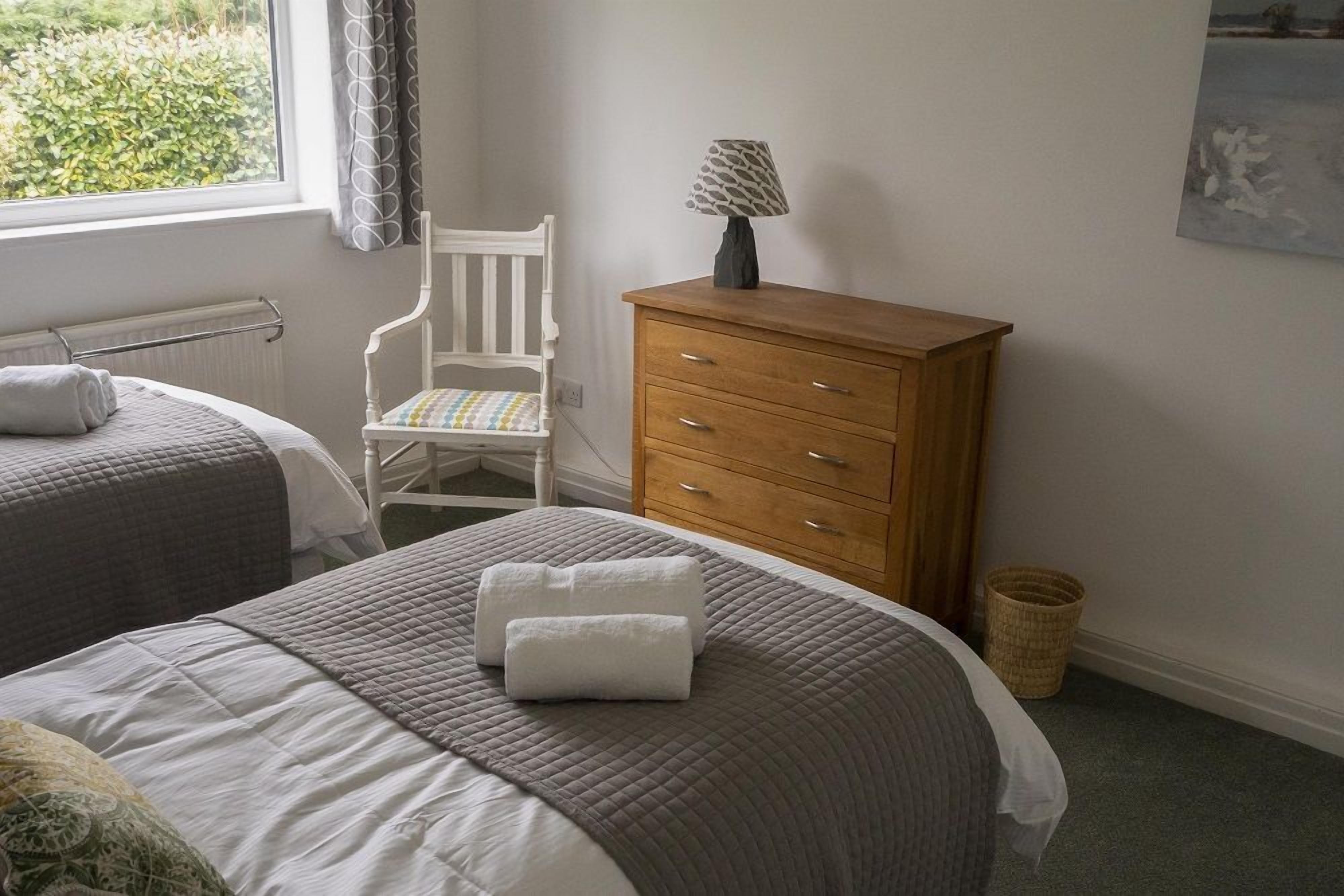 Una camera da letto con due letti, una cassettiera in legno, una sedia e una lampada.