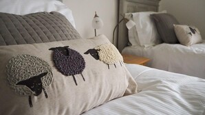 A neatly made bed with a pillow featuring a knitted sheep design.
