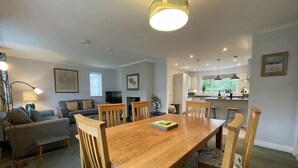 A modern living room with a wooden dining table, grey sofas, and a TV.