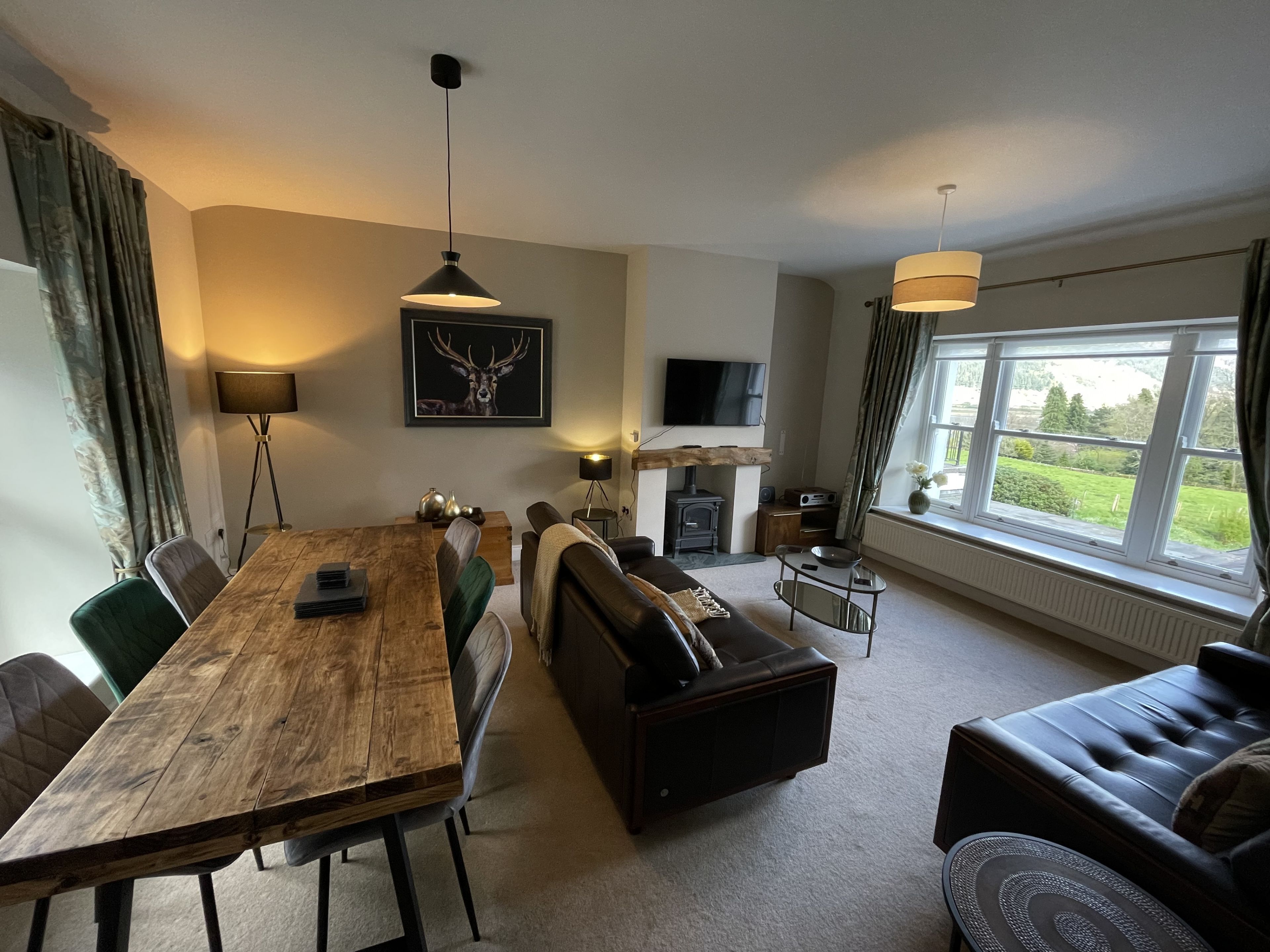 A cozy living room with a wooden dining table, a sofa, and a TV mounted on the wall.