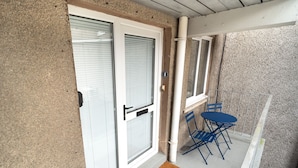 Un balcon avec une porte, une fenêtre et une table pliante bleue.