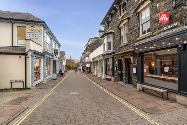 A street view with shops on either side, a clear sky, and a pedestrian crossing.