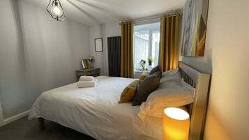 A neatly made bed with pillows, a bedside table with a lamp, and a window with curtains.