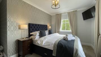 A neatly made bed with a dark headboard, a bedside table with a lamp, and a window with curtains.