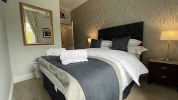 A neatly made bed with white linens and a grey and white striped blanket, a bedside table with a lamp, and a patterned wall.