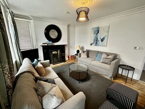 A living room with a fireplace, a sofa, a coffee table, and a striped ottoman.