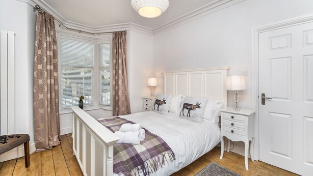 Ein Schlafzimmer mit einem Bett, Nachttischen, einer Bank, einem Fenster mit Jalousien und einer Tür.
