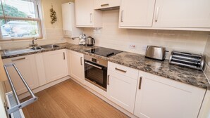 A modern kitchen with white cabinets, a granite countertop, a built-in oven, a toaster, and a window with blinds. - 11 Howrah's Court -  an apartment that sleeps 4 guests  in 2 bedrooms (Central Keswick)