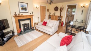 A living room with a fireplace, a sofa, a dining table, and a kitchen visible in the background. - 11 Howrah's Court -  an apartment that sleeps 4 guests  in 2 bedrooms (Central Keswick)