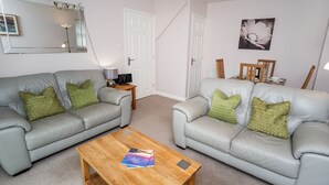 A living room with two grey leather sofas, a wooden coffee table, a side table with a lamp, and a framed picture on the wall.