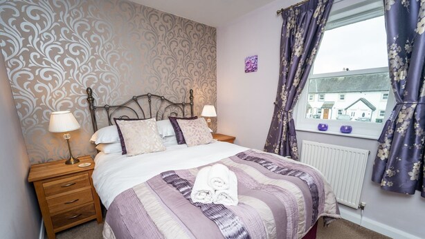 A bedroom with a bed, two bedside tables, a window with curtains, and a radiator.