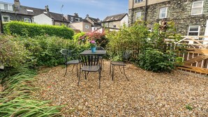 Eine Terrasse mit Tisch und Stühlen, umgeben von Kies, mit Garten und einem Steinhaus im Hintergrund.