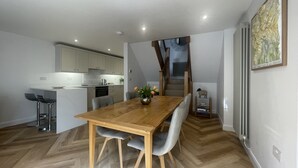 A modern kitchen with white cabinets, a wooden dining table, and grey upholstered chairs. - Daisy Cottage -  a cottage that sleeps 4 guests  in 2 bedrooms (Central Keswick)