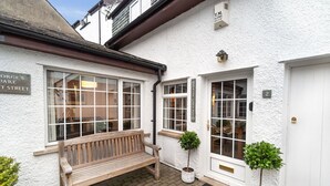 A white building with a wooden bench outside, a door labeled "Daisy Cottage," and a sign for "T.M. ALARMS." - Daisy Cottage -  a cottage that sleeps 4 guests  in 2 bedrooms (Central Keswick)