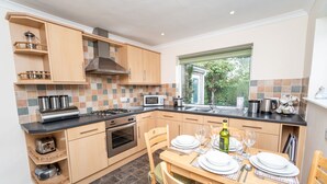 Een moderne keuken met houten kastjes, een gasfornuis, een magnetron en een eethoek voor vier personen met een tafel en stoelen.