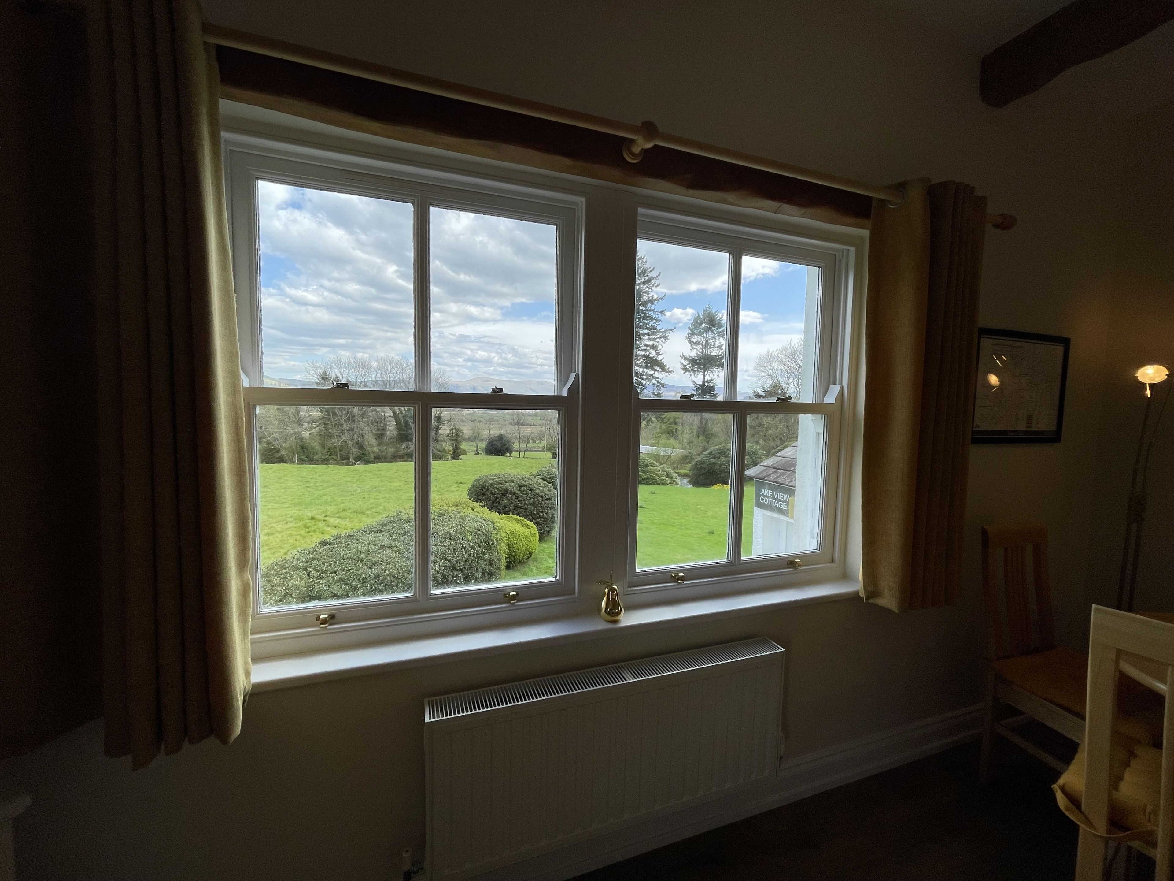 Et værelse med et stort vindue, der giver udsigt over en have, og et skilt med teksten "Lake View Cottage".