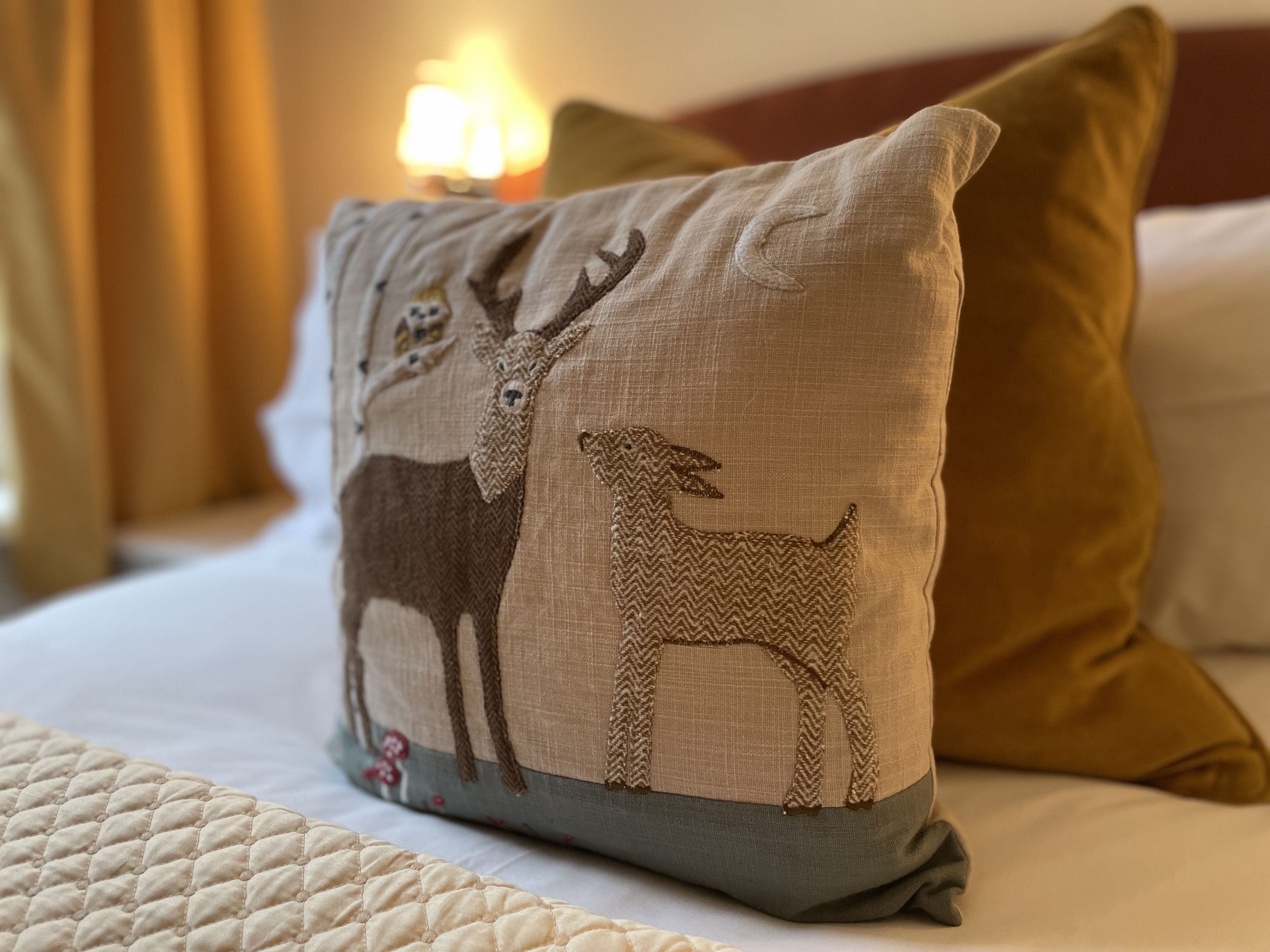 Una cama con un edredón acolchado, un almohadón con diseño de ciervo y un almohadón verde.