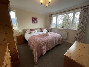 A bedroom with a bed, a nightstand, a dresser, a window with curtains, a radiator, and a chandelier.