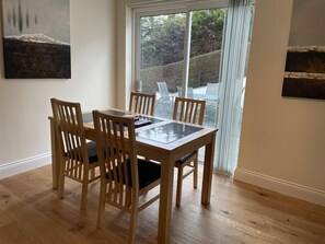Un coin repas avec une table en verre et des chaises en bois, une porte-fenêtre coulissante donnant sur l’extérieur et des œuvres d’art accrochées aux murs.