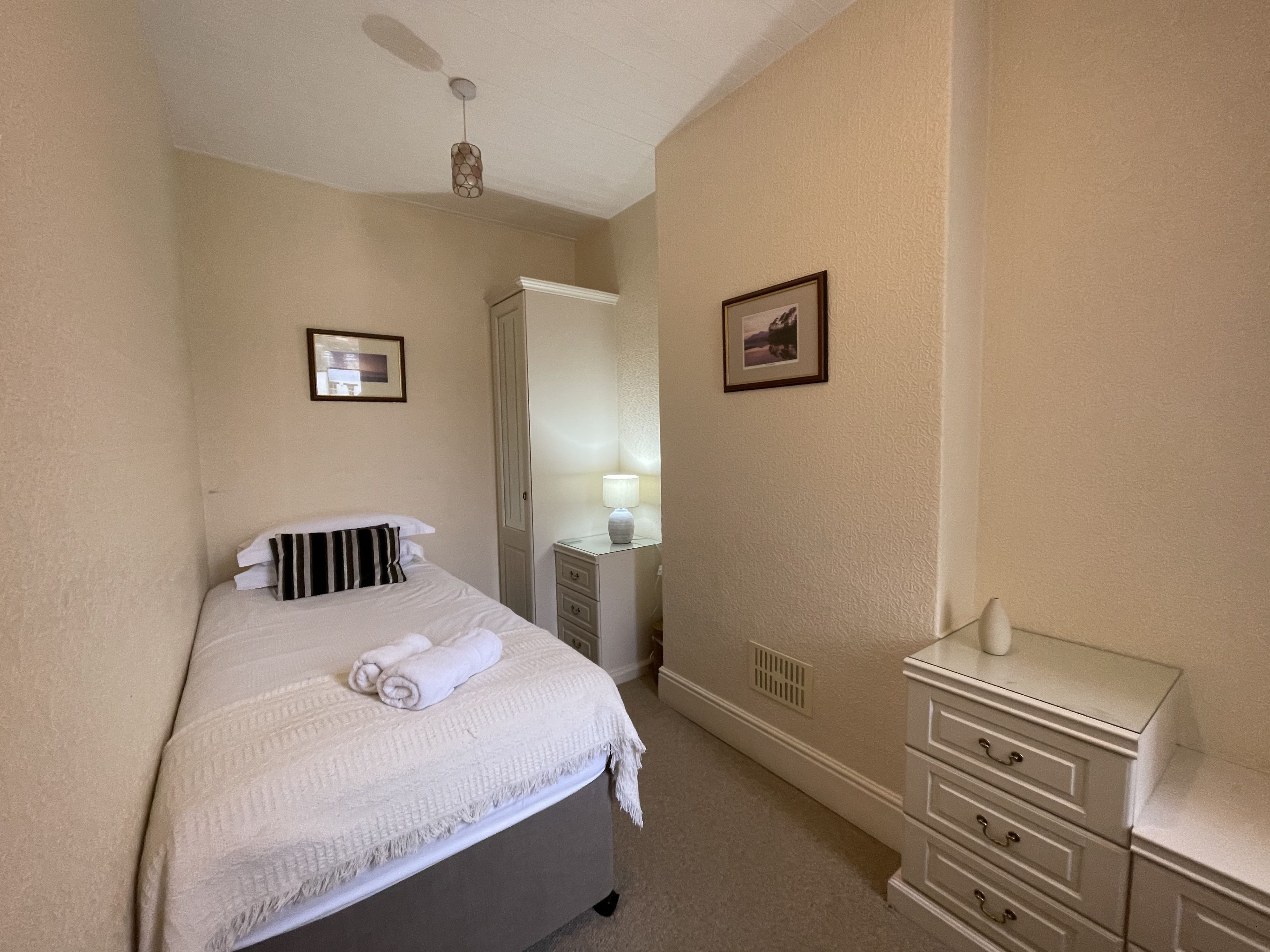 A neatly arranged bedroom with a bed, bedside table, and a dresser.