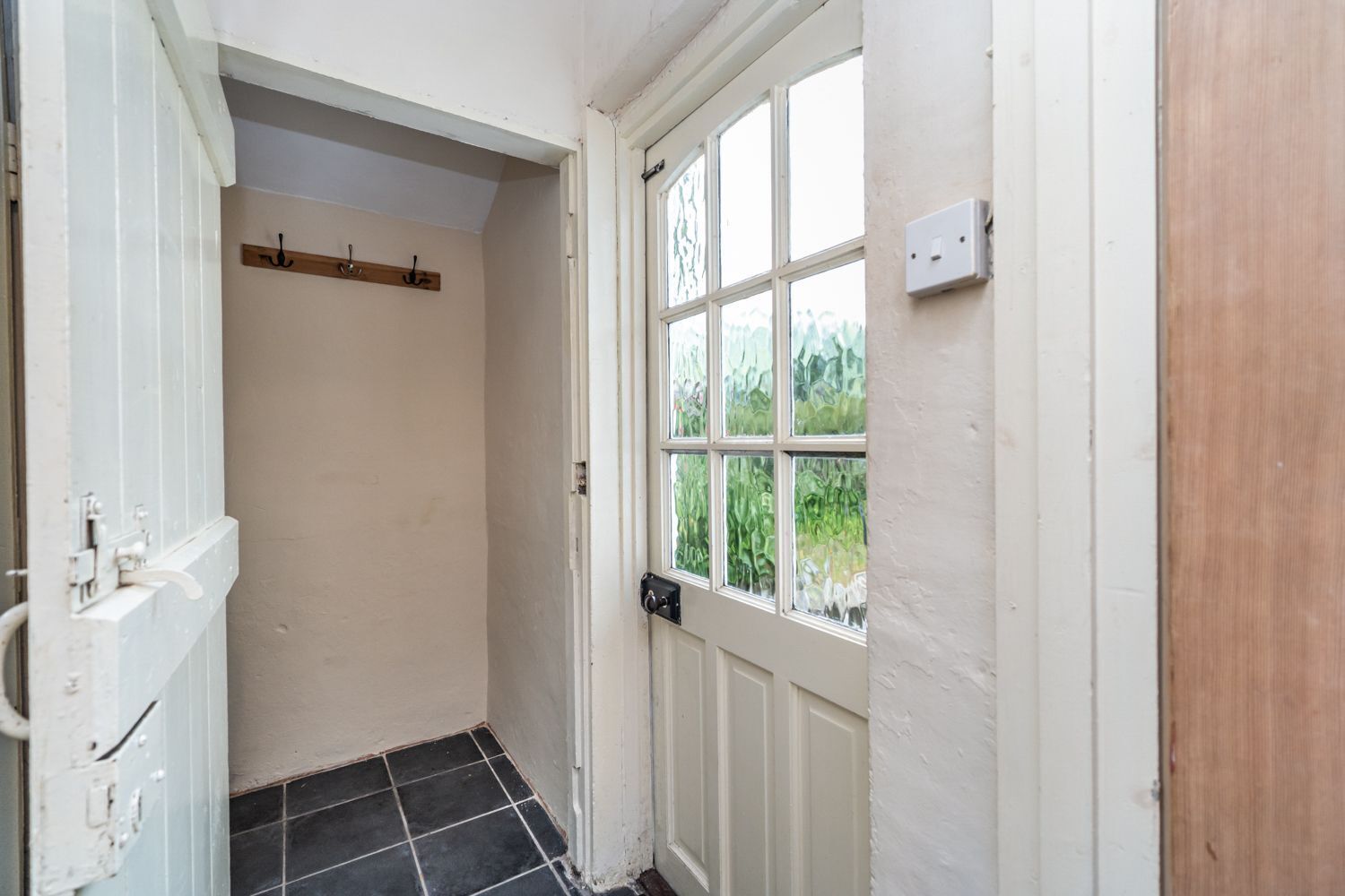 A narrow hallway with a white door and a window with a view of greenery.
