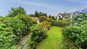 Un sendero en un jardín que conduce a una casa, con un camino de piedra y abundante vegetación.