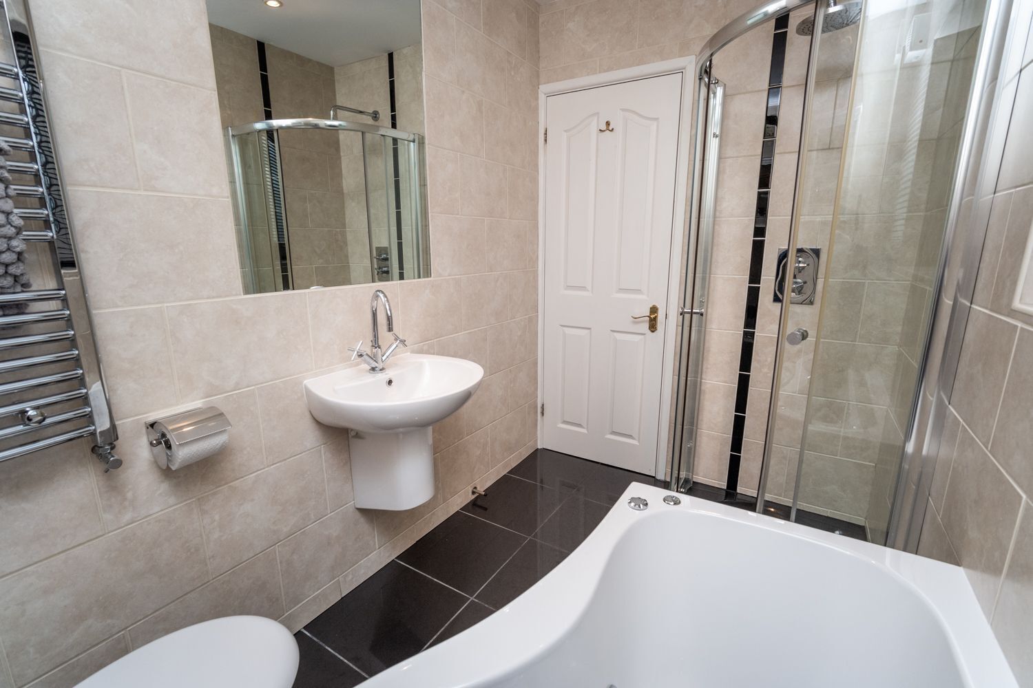 Un baño moderno con una bañera blanca, un lavabo, una cabina de ducha de vidrio y una puerta.