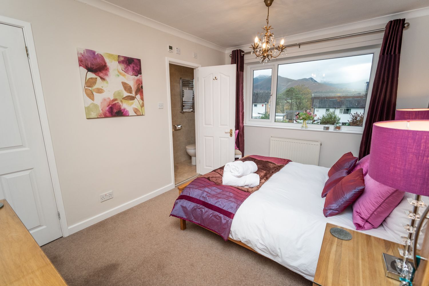 A bedroom with a bed, a window with a view, a chandelier, and a painting on the wall.