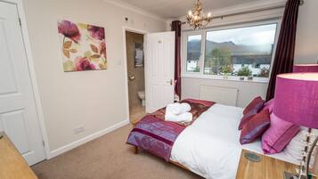A bedroom with a bed, a window with a view, a chandelier, and a painting on the wall.