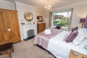 Ein Schlafzimmer mit Bett, Schrank, Kamin und Fenster mit Blick auf Grünflächen.