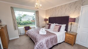 A bedroom with a large bed, two bedside tables with lamps, a dresser, a window with curtains, and a view of the outside. - Appletree -  a house that sleeps 6 guests  in 3 bedrooms (Portinscale)