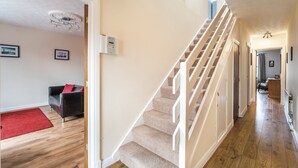 A staircase with beige carpeted steps and white railings, leading to a room with a red carpet and a black leather sofa. - Alban Rise -  a maisonette that sleeps 5 guests  in 3 bedrooms (Central Keswick)