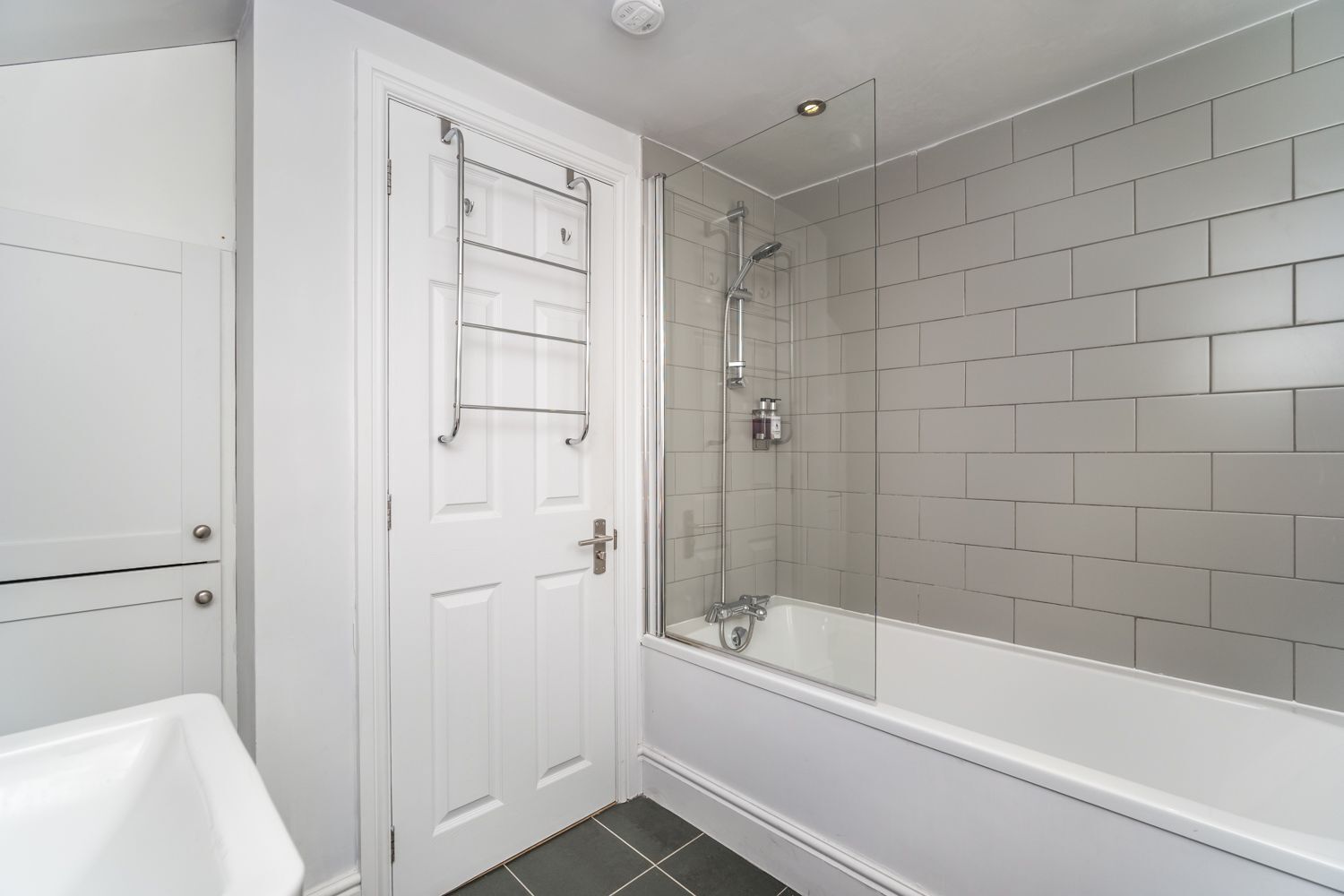 Een badkamer met een witte badkuip, een douche en een deur met een handdoekhouder.