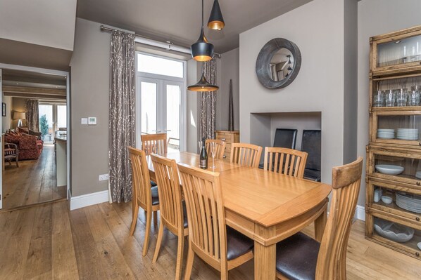 Un coin repas avec une table et des chaises en bois, un luminaire suspendu, une cheminée et un meuble vitré où sont exposées de la vaisselle.