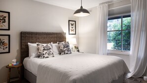 Ein Schlafzimmer mit einem großen Bett, einem Rattan-Kopfstück, einer Hängelampe und einem Fenster mit Vorhängen.