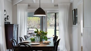 Ein Esszimmer mit Holztisch, schwarzen Stühlen, einer Hängelampe und Blick ins Freie durch große Fenster.