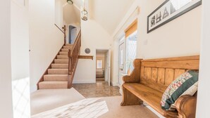 A spacious hallway with a wooden staircase, a wooden bench, and a framed picture on the wall.