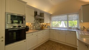 A kitchen with white cabinetry, a built-in oven, a window with a view, and a countertop with various kitchen items.