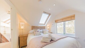 A bedroom with a skylight, a bed with a pink blanket, a nightstand, and a window with a view of trees.