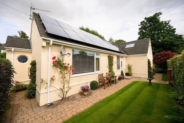 A house with solar panels, a garden, and a patio with chairs.