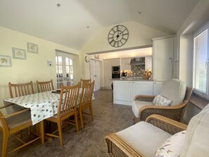 A dining area with a table and chairs, a kitchen with white cabinets, and a wicker chair.