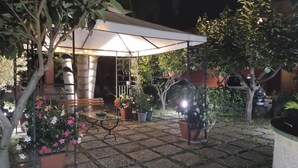 A covered patio area with a table and chairs, surrounded by potted plants and a white canopy.