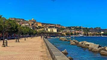 Um calçadão costeiro com um pavimento de pedra, vista para o mar e edifícios ao fundo.