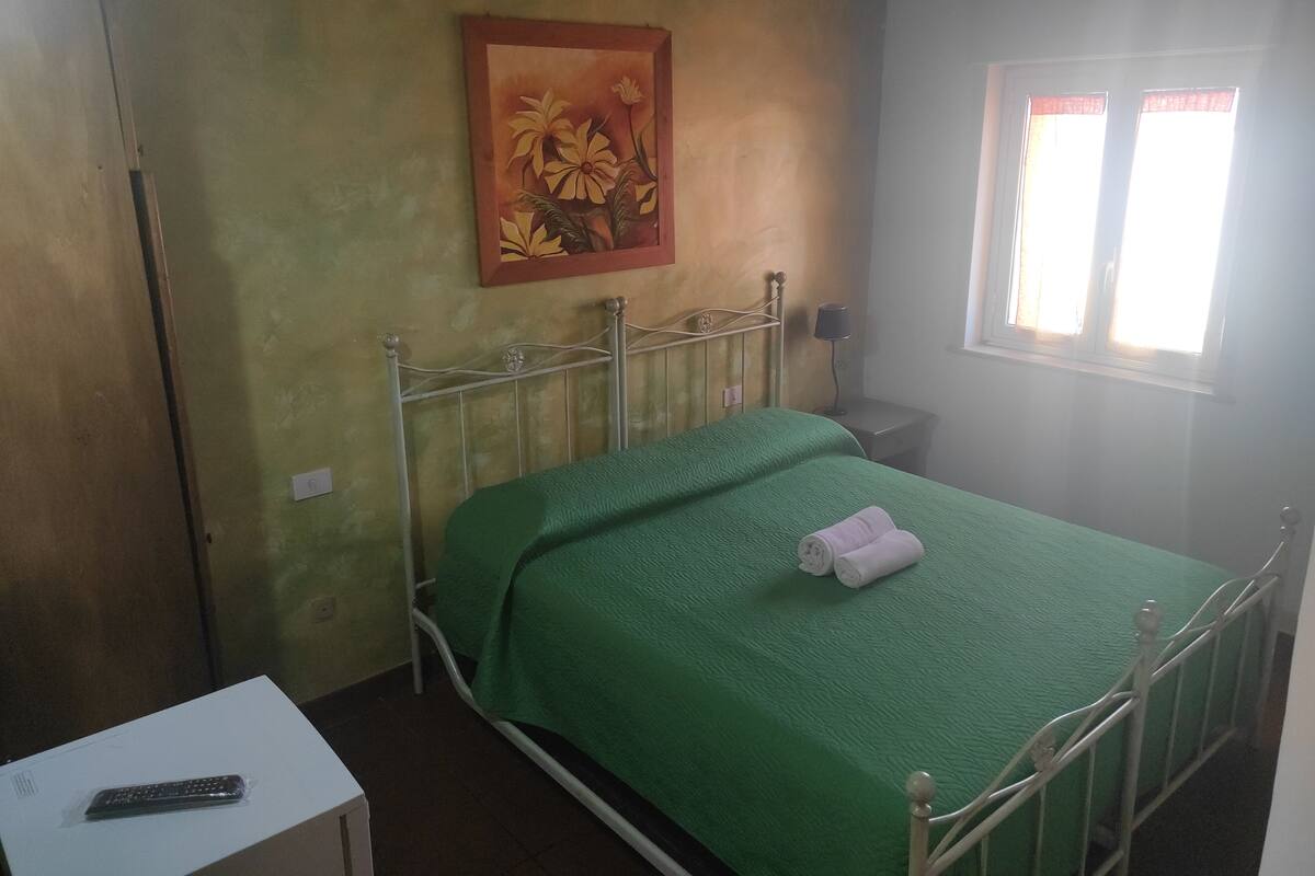 Une petite pièce simple, avec un lit simple, une table de chevet, une lampe et un tableau accroché au mur.