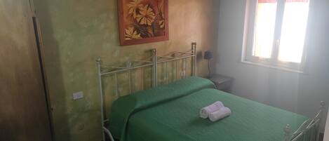 Una habitación pequeña y sencilla con una cama individual, una mesita de noche, una lámpara y un cuadro en la pared.