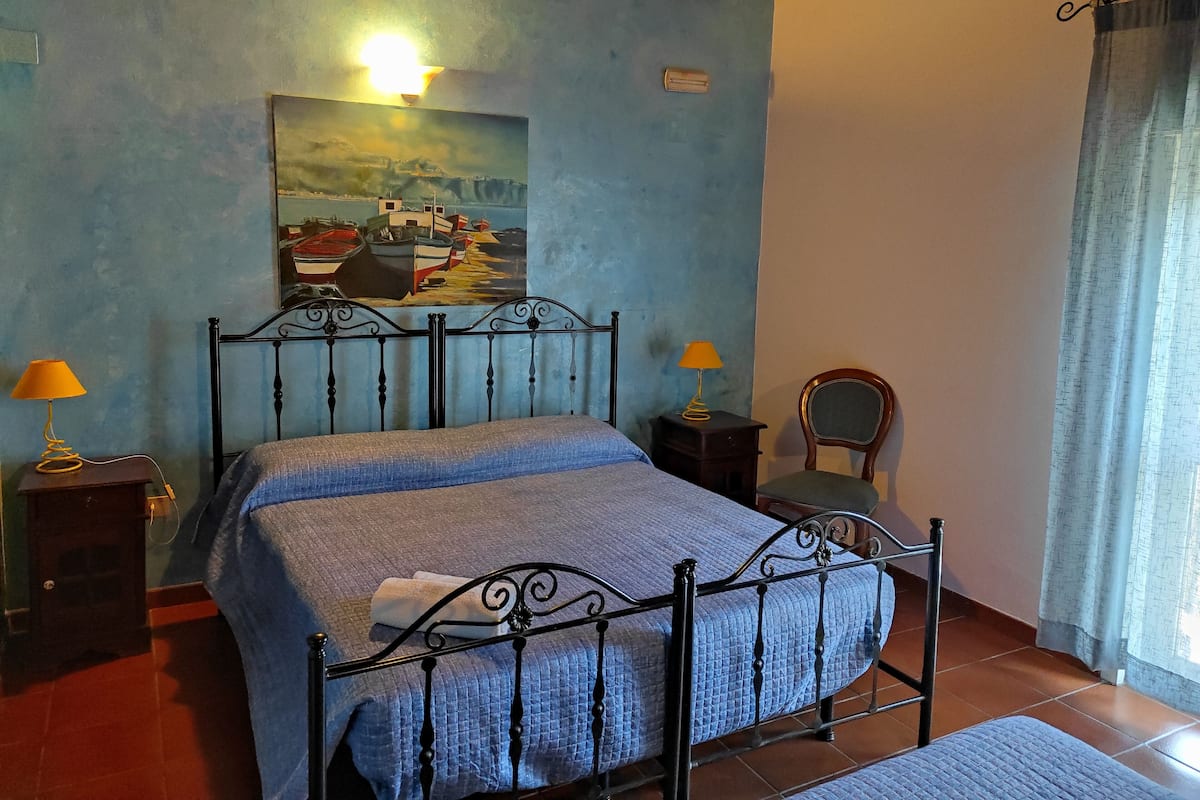 Une chambre à coucher avec un lit, deux lampes de chevet, une chaise, un tableau au mur et une fenêtre avec des rideaux.