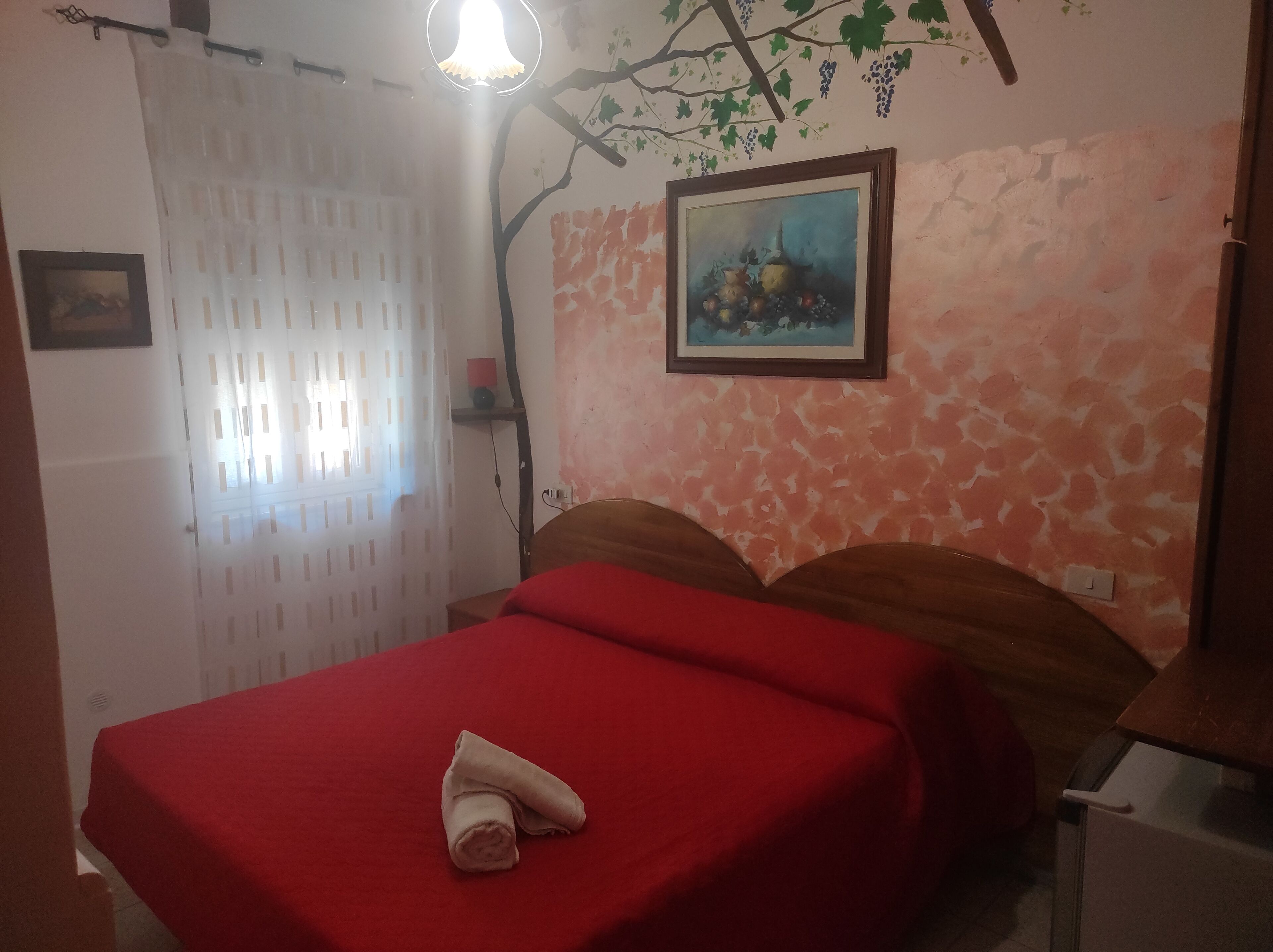 Une pièce comprenant un lit, un tableau, une fenêtre avec des rideaux et un mur orné d’un motif texturé.