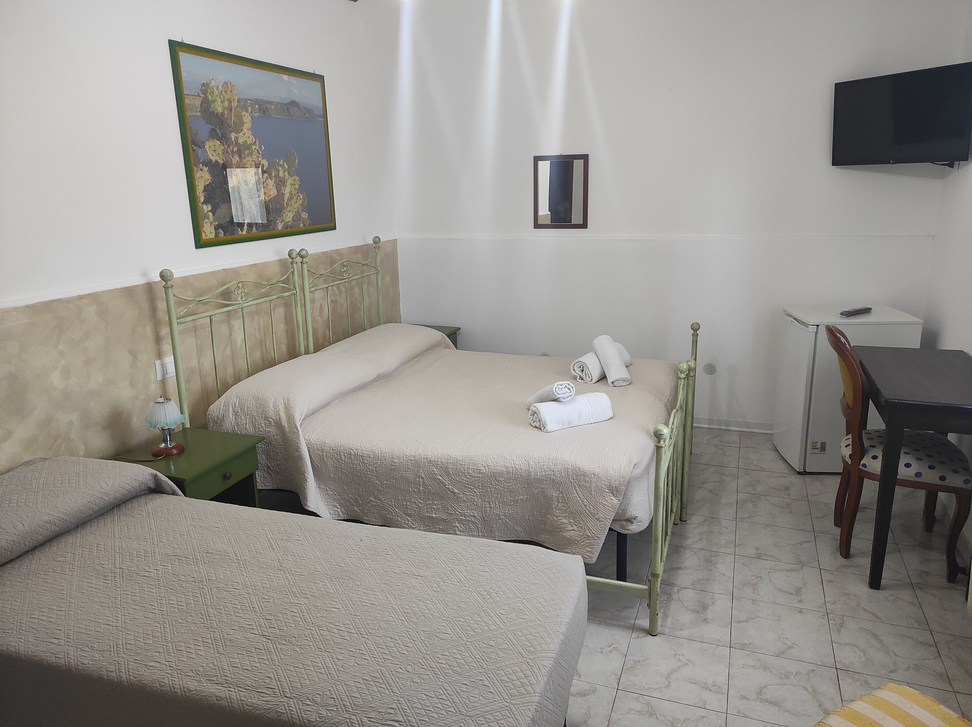 Quarto de hotel com duas camas, uma escrivaninha, uma cadeira, uma televisão e um quadro na parede.